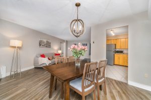 Cozy dining area with wooden table, chairs, and floral centerpiece under modern chandelier.