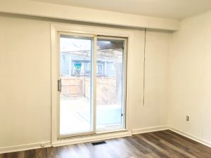 Bright empty room with large sliding glass door and wood flooring.