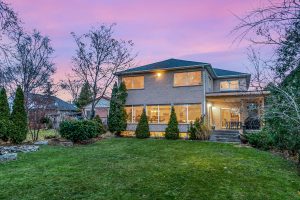 Two-story house with illuminated windows at dusk and a spacious lawn.