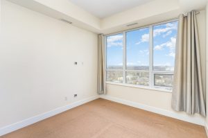 Empty bedroom with beige carpet and large window with curtains.