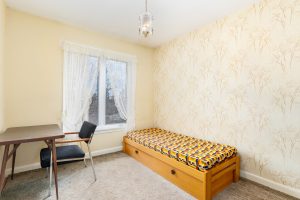 Small bedroom with single bed and desk by window.