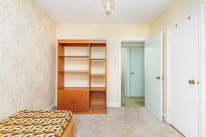 Empty bedroom with a wooden bookshelf and open bathroom door.